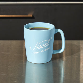 Blue ceramic coffee mug with Novel Coffee Roasters logo.