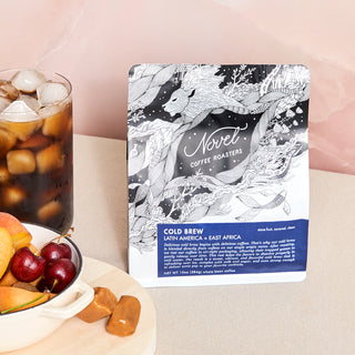 A bag of Cold Brew coffee beans next to a glass of ice filled with Cold Brew and a bowl of summer fruit and caramels. 